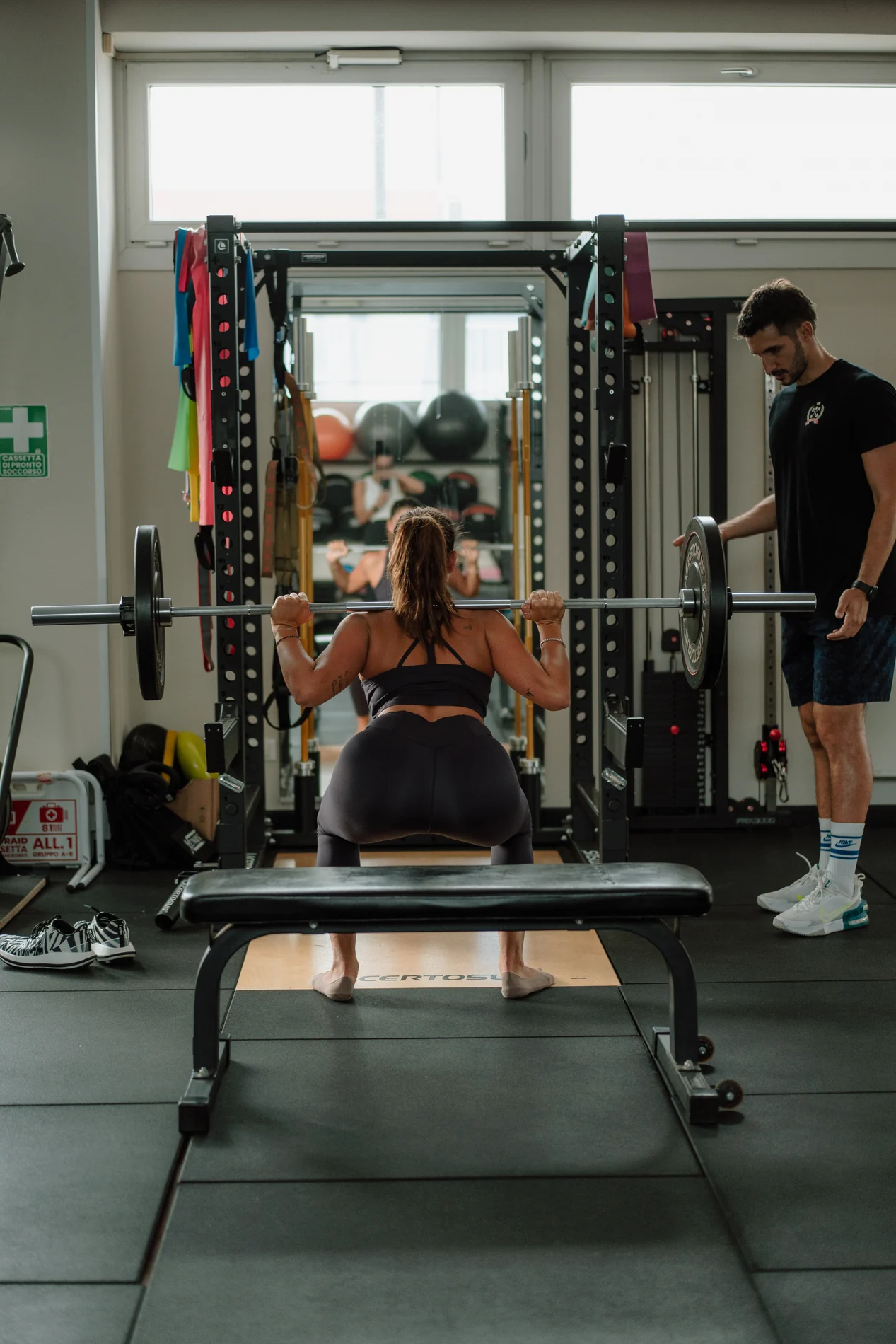 Una donna si allena con il bilanciere mentre un coach BorgoFit la segue